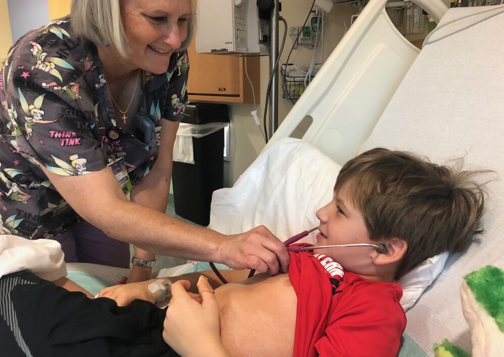 A nurse lets a boy listen to her stethoscope.