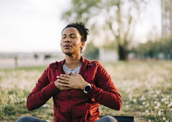 A woman performs a breathing exercise outdoors.