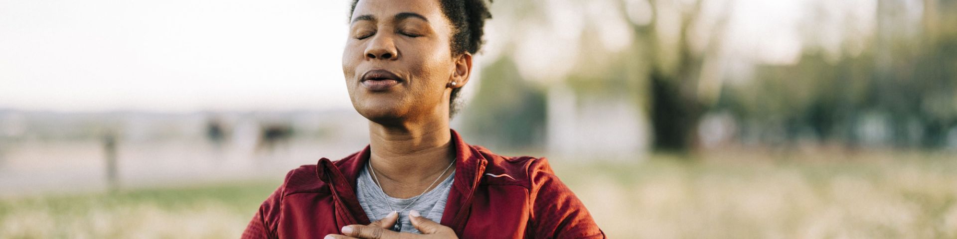 A woman performs a breathing exercise outdoors.