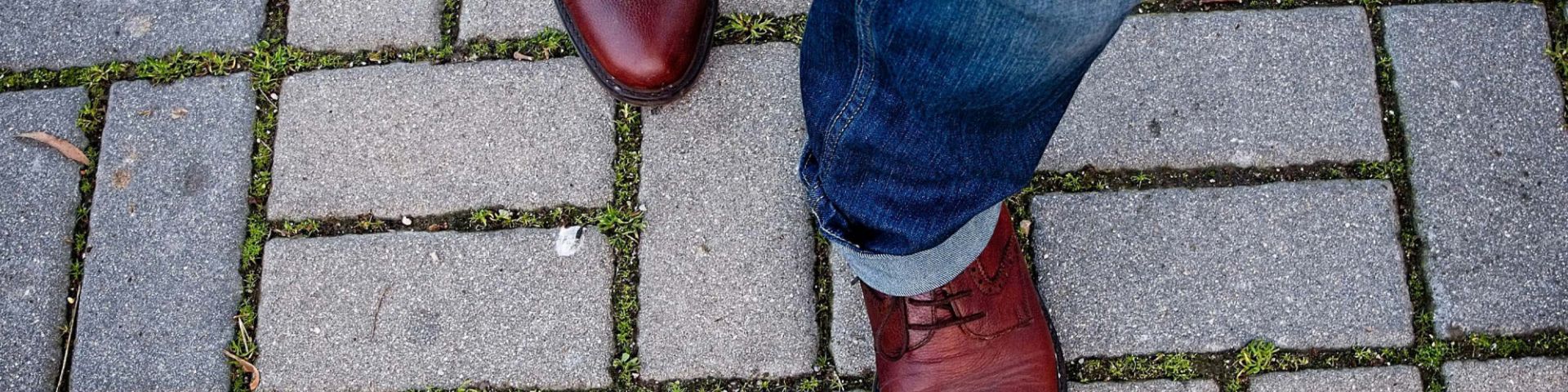 A man's feet walk on a sidewalk.
